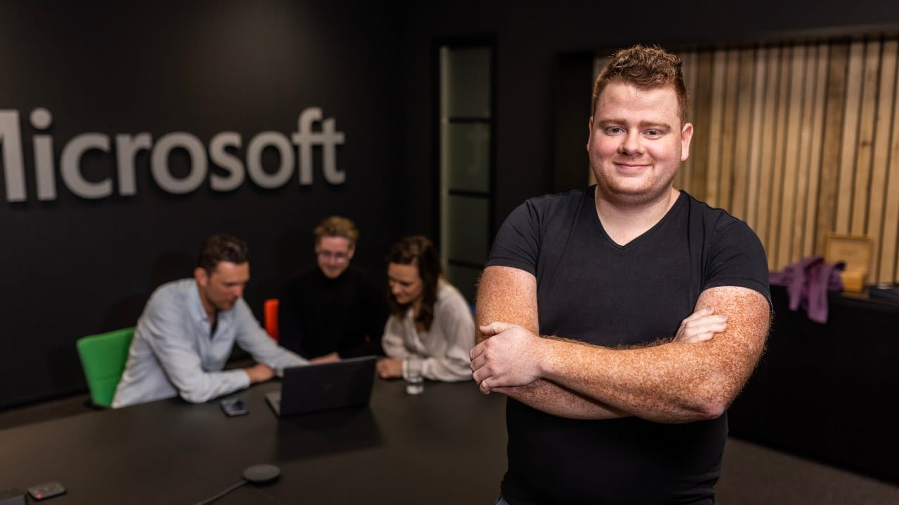 IT Consultant staat in ruimte met Microsoft logo op de achtergrond